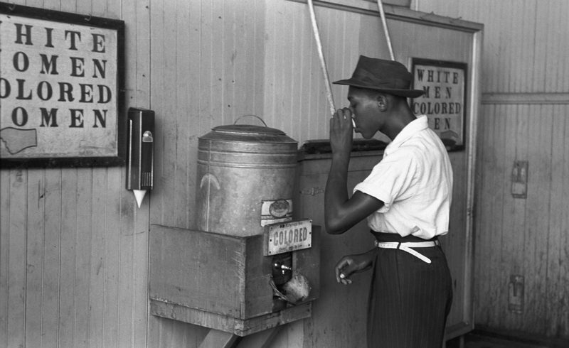 An African-American man drinking from a racially segregated water cooler marked "Colored", in Oklahoma City c. 1939.