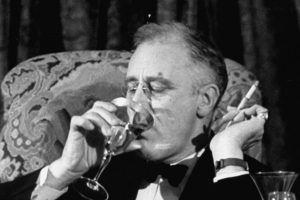 US president F.D.Roosevelt sitting on a sofa, sipping a martini, and holding a cigarette in the other hand.