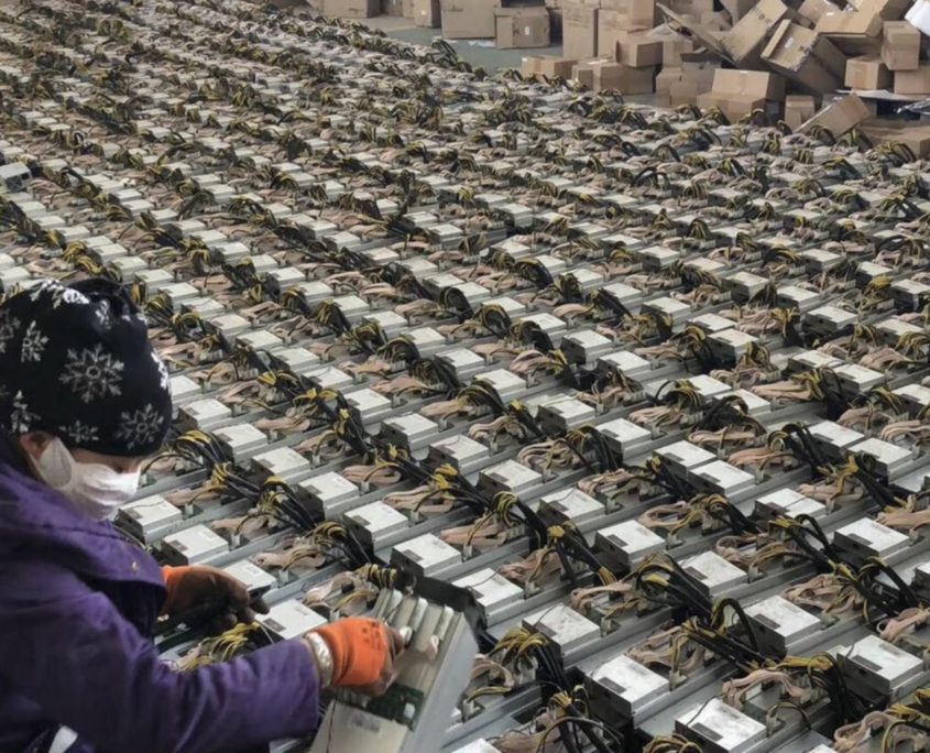 Female worker wearing gloves sits in front of numerous bitcoin mining machines ready to be shipped